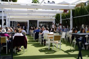 Comensales disfrutando en la terraza del Kiosco de las Flores, en C. Betis, Sevilla, durante un día soleado.